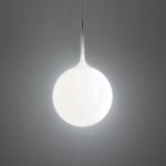 Artemide Castore suspension lamp, hand blown opal glass sphere with a tapered white glass neck and slim cable suspension, illuminated against a dark gray backdrop, three quarter view.
