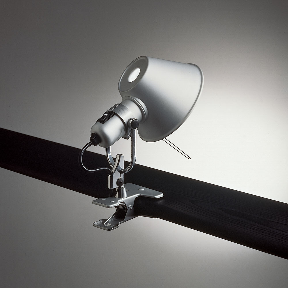 Artemide Tolomeo clip task lamp in polished aluminum, conical shade head mounted directly on a metal spring clip clamped to a black bar, three quarter view.